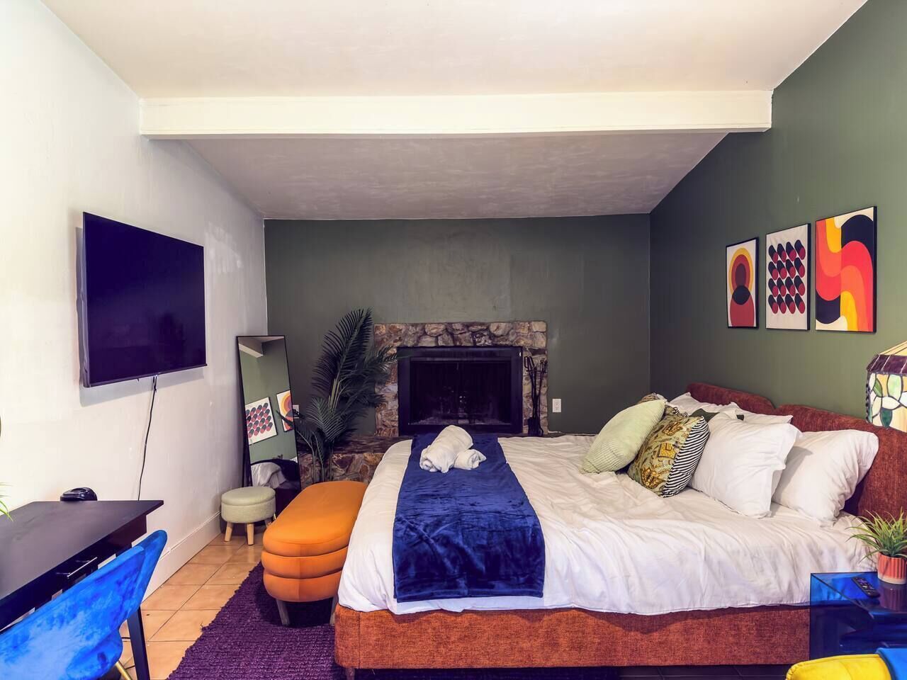 A bedroom with a bed, a TV, a fireplace, and artwork on the wall.