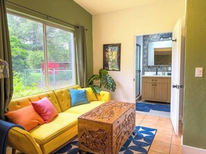 A living room with a yellow sofa, a coffee table, and a large window. - Retro-Chic 4BR House w/ yard Downtown Gainesville (Gainesville)