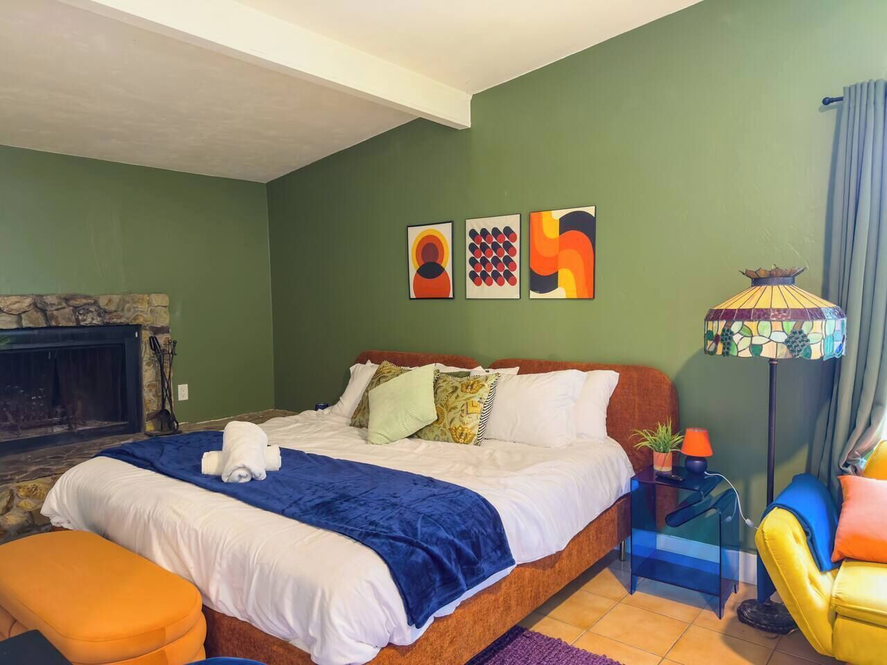 Een hotelkamer met een bed, een nachtkastje, een lamp, een stoel en een open haard.