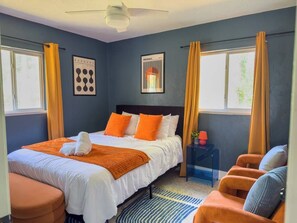 A hotel room with a bed, two chairs, a nightstand, and a window with curtains. - Retro-Chic 4BR House w/ yard Downtown Gainesville (Gainesville)
