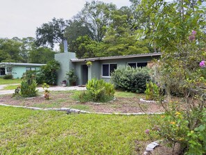 A residential property with a single-story house, a front yard with various plants, and a visible chimney. - Retro-Chic 4BR House w/ yard Downtown Gainesville (Gainesville)