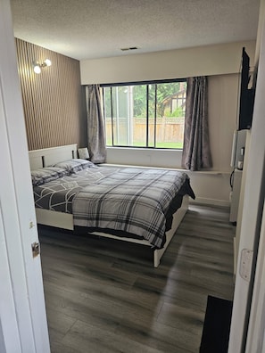 A bedroom with a bed, a window with curtains, and a view of the outside.