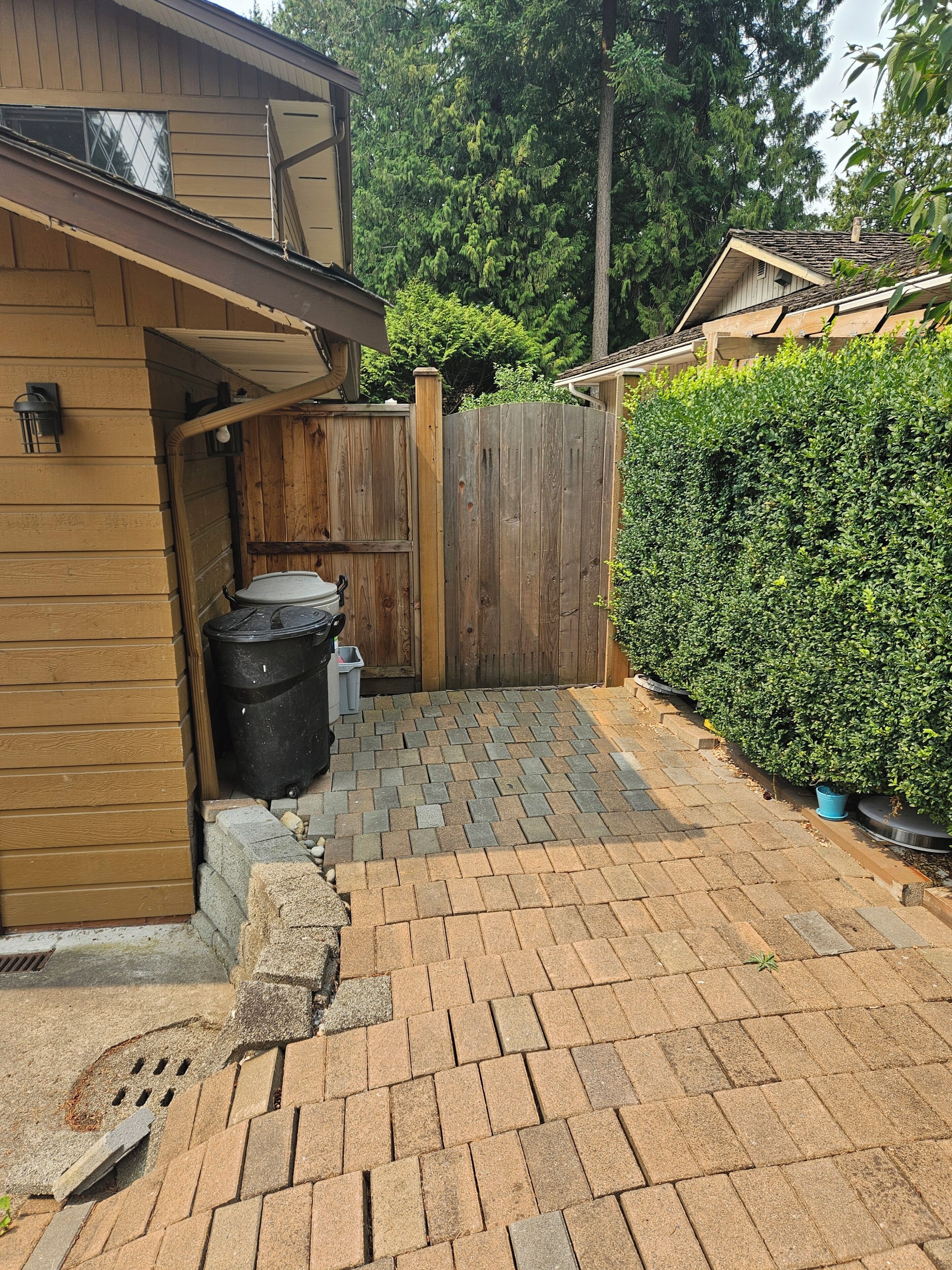 A backyard with a wooden shed, a black trash bin, and a paved patio.