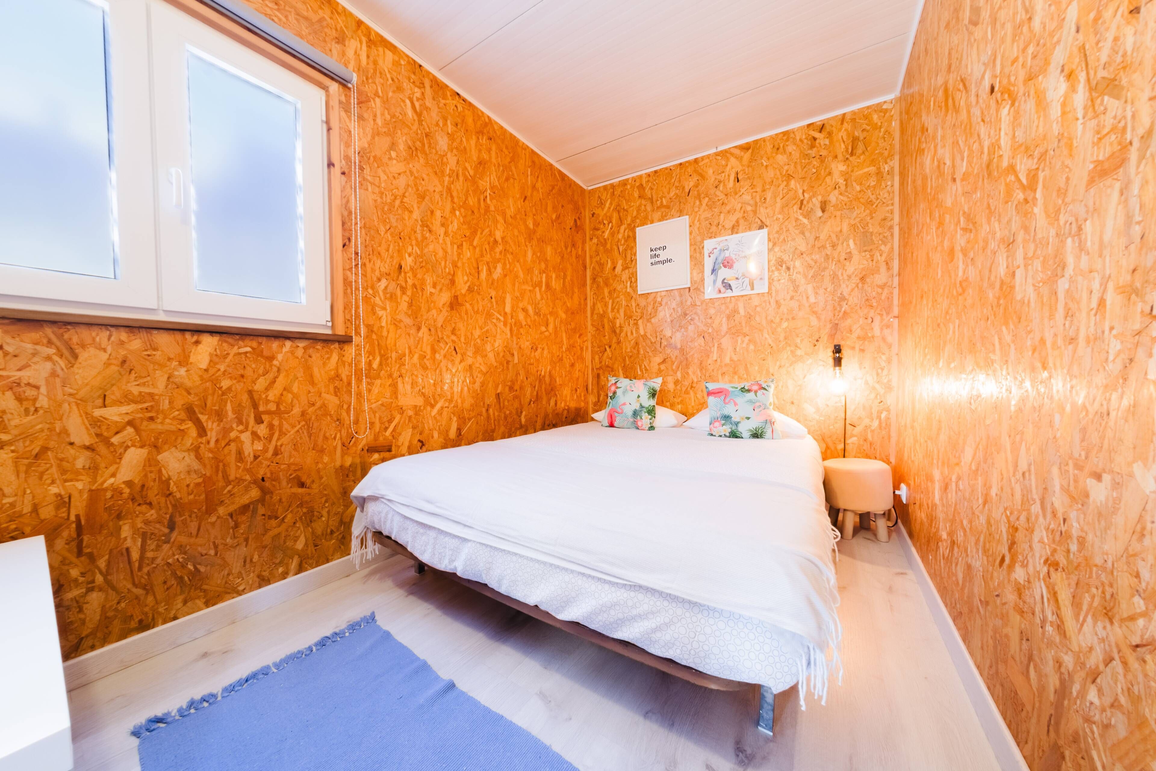 A bedroom with a bed, a bedside table, a lamp, and a window.