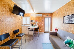 A compact room with a kitchenette, a flat-screen TV, a sofa, and a fire extinguisher. - Bungallow - Pátio Mariano (Peniche)
