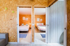 Habitación con dos camas, paredes de madera y una puerta que da a otra habitación.