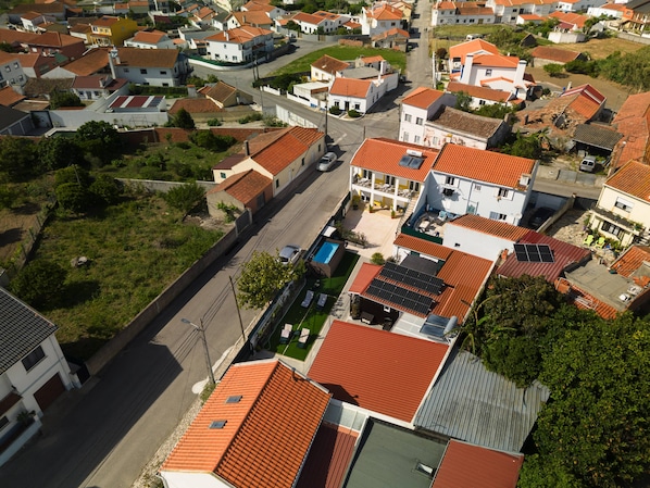 An aerial view of a residential area with houses featuring red-tiled roofs, a central road, and a swimming pool.