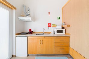 Uma cozinha compacta com pia, micro-ondas, cafeteira e um refrigerador pequeno.