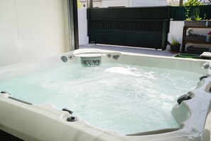 Een jacuzzi met ingebouwde verwarming, omgeven door een witte muur en een donker hek.