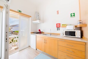 A modern kitchen with a microwave, sink, and cabinets. - II Ninho - Pátio Mariano (Peniche)