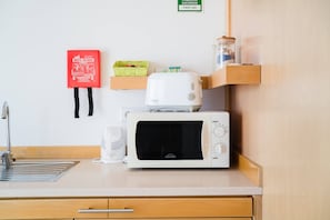 Een kitchenette met een magnetron, broodrooster en een rode brandblusser aan de muur.