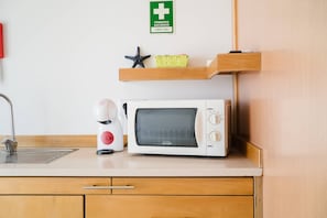 Eine Küchenzeile mit Mikrowelle, Kaffeemaschine und einem Regal mit einem Erste-Hilfe-Schild.