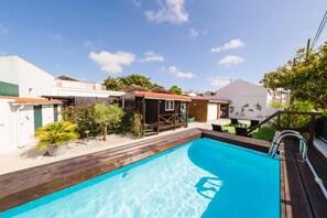 A swimming pool with a wooden deck, surrounded by houses with white walls and red roofs. - III Ninho - Pátio Mariano (Peniche)