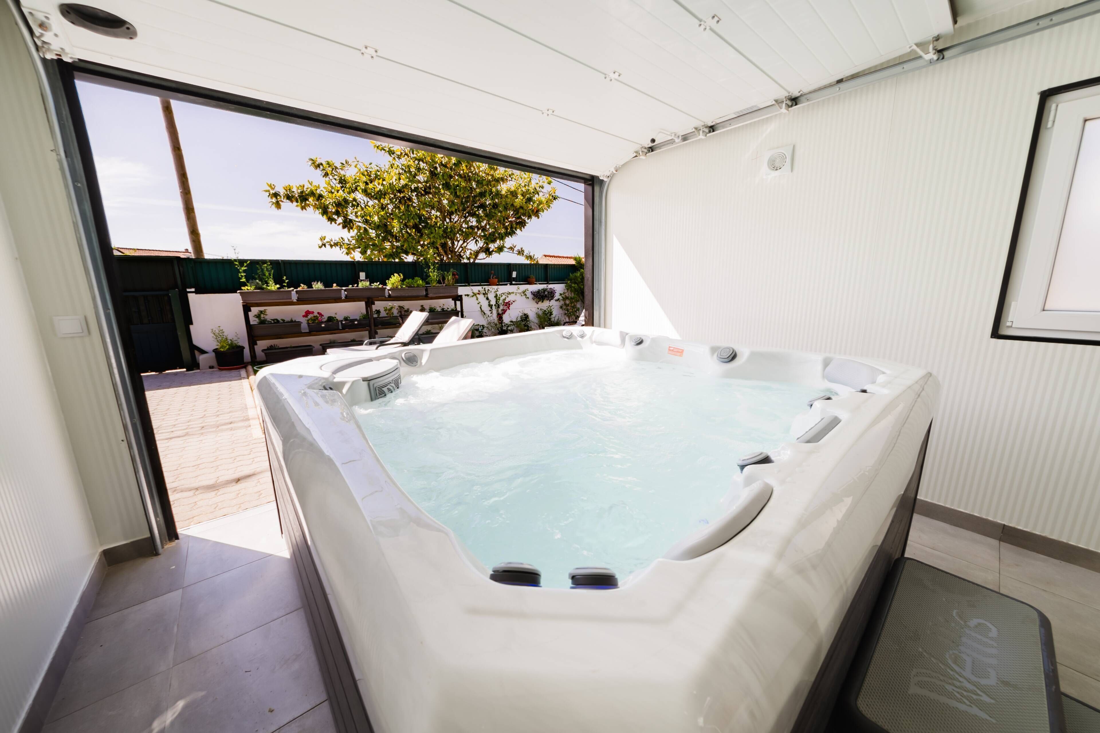 A hot tub with a view of a garden and a building in the background.