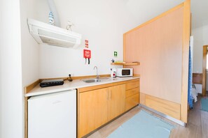 A compact kitchenette with a microwave, sink, and a small refrigerator. - III Ninho - Pátio Mariano (Peniche)
