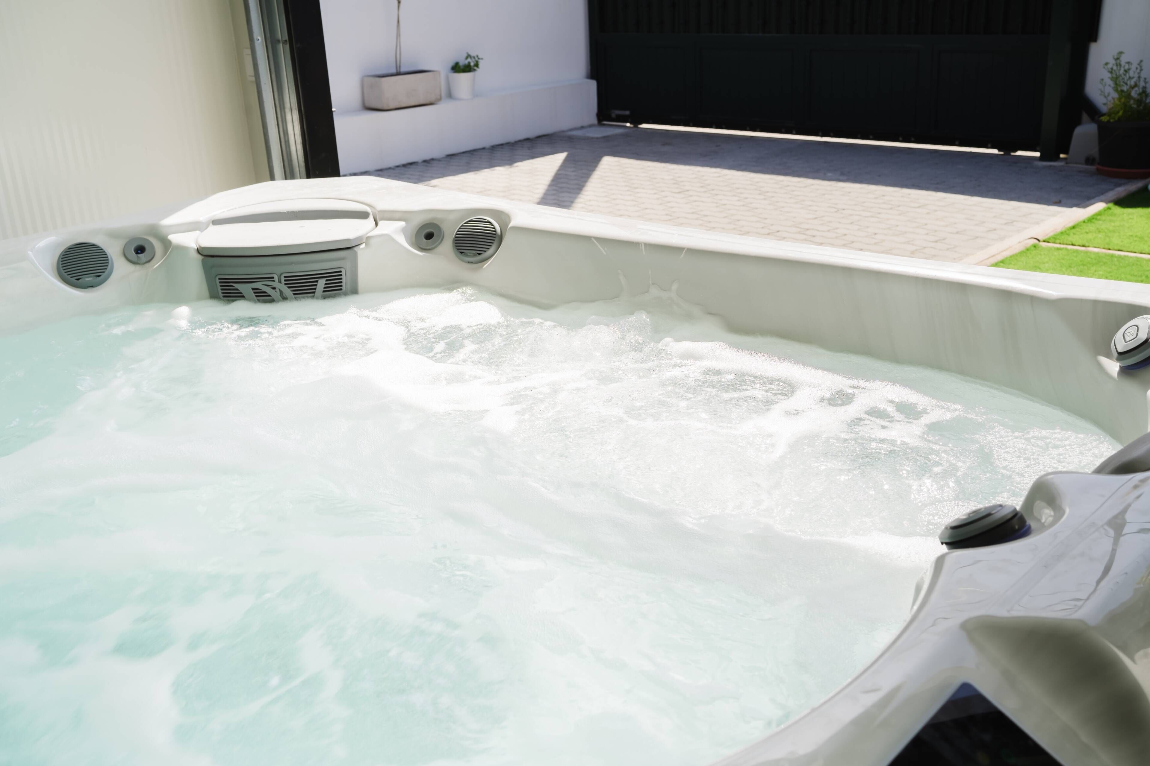 Een jacuzzi met een witte buitenkant, een bedieningspaneel en een kleine plant in een pot aan de muur.