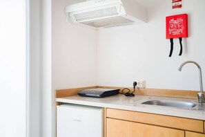 A kitchen with a white countertop, a sink, a dishwasher, a red fire extinguisher, and a ceiling vent.
