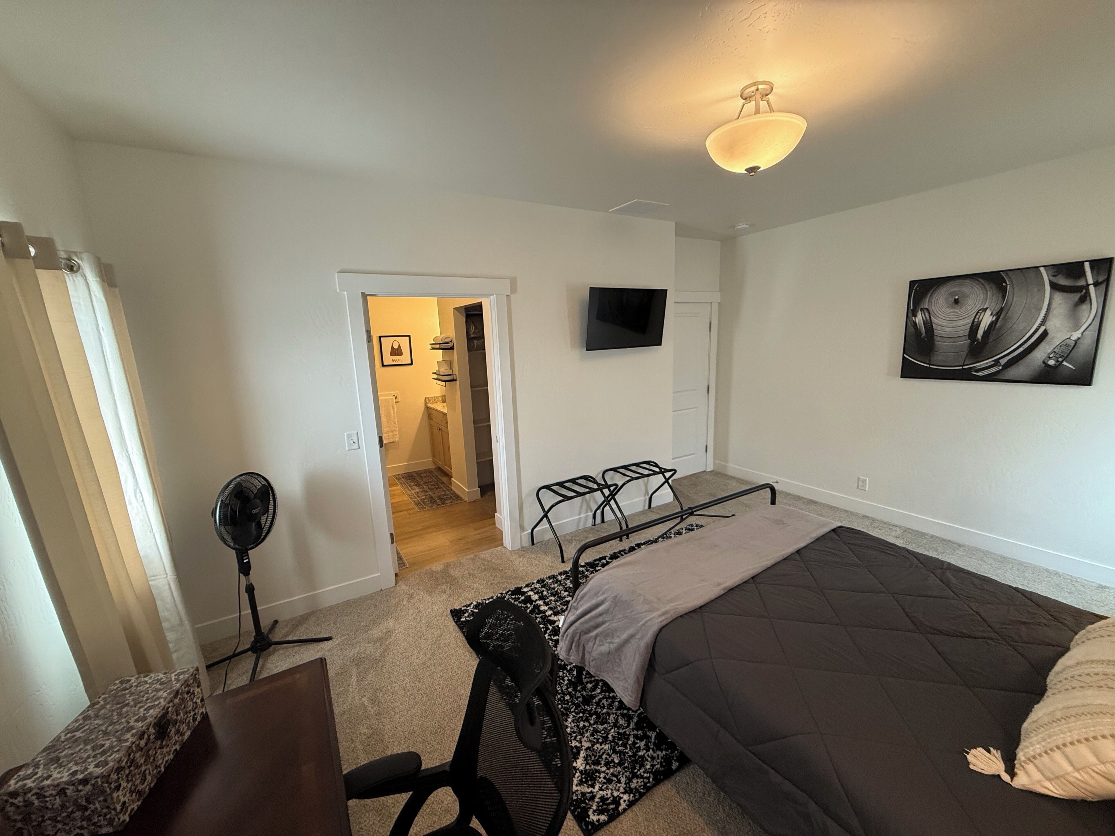 A bedroom with a bed, a desk, a chair, a TV, and a door leading to a bathroom.