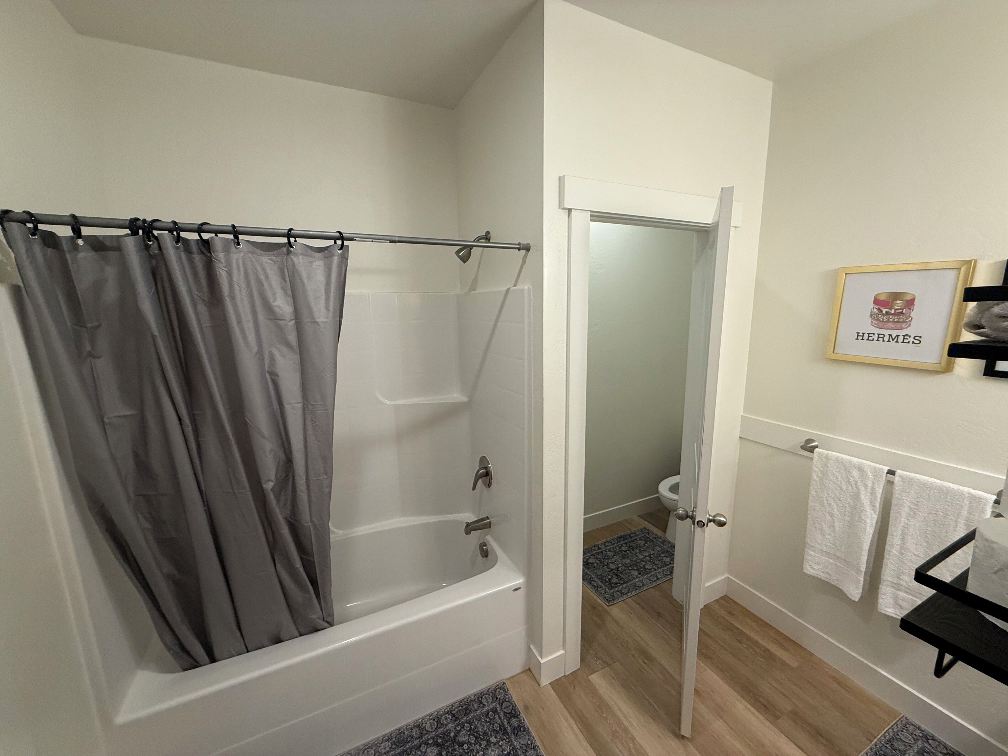 Un baño con bañera, cortina de ducha, inodoro y un cuadro en la pared.