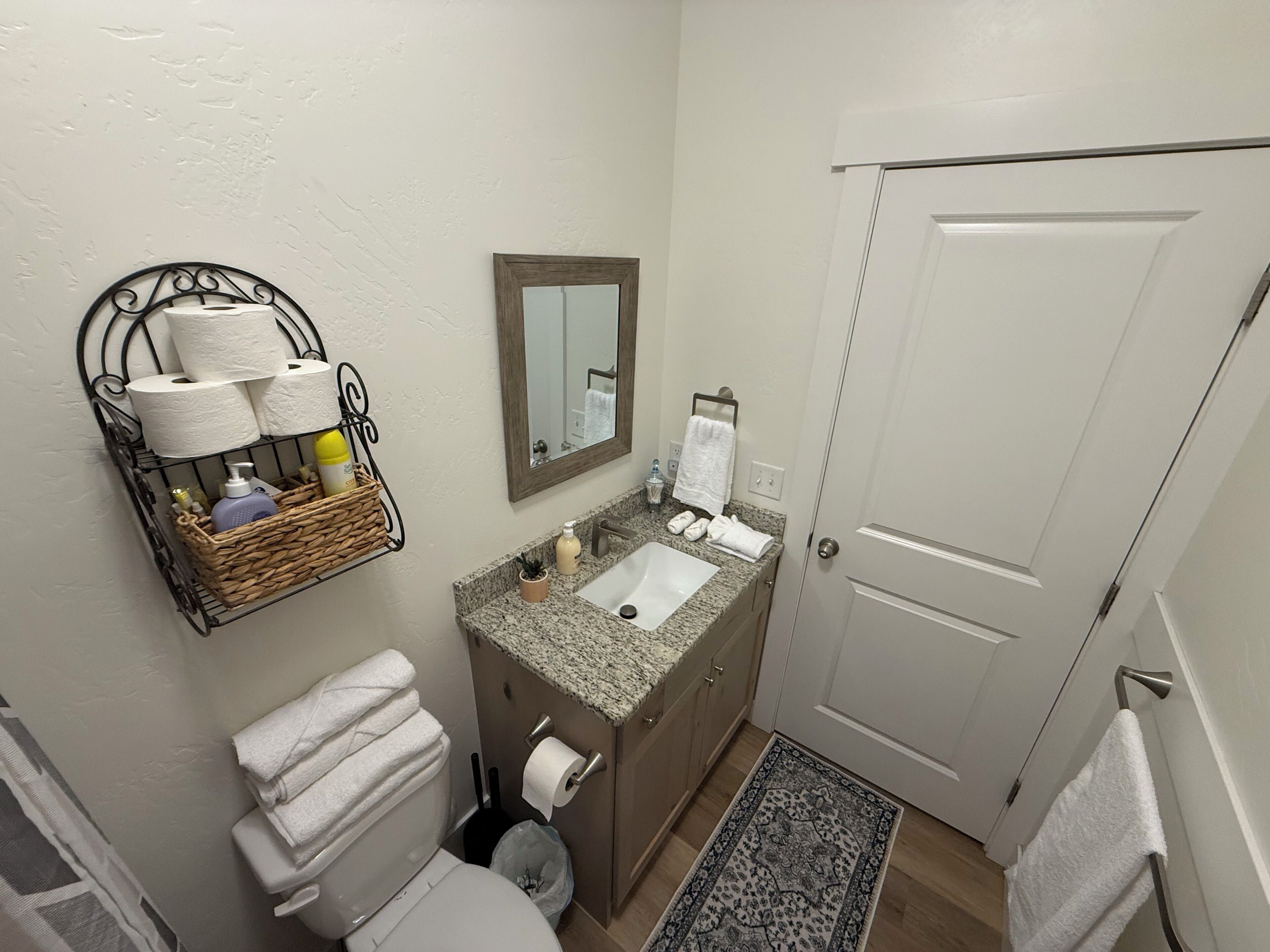 A bathroom with a toilet, sink, and a mirror. There is a basket with toiletries and towels on the wall.