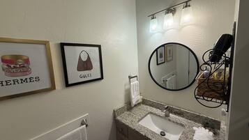 Un baño con un bolso Gucci enmarcado, un artículo Hermes enmarcado, un espejo redondo y un perchero para toallas.