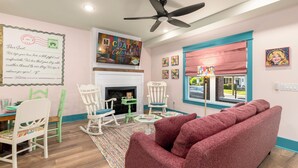 A cozy living room with a fireplace, a ceiling fan, and a large window with a view. - 2BR/2BA Hot Tub Suite • Coat of Many Colors (Sevierville)