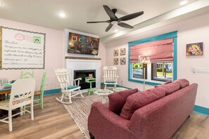 A cozy living room with a fireplace, a ceiling fan, and a large window with a view. - 2BR/2BA Hot Tub Suite • Coat of Many Colors (Sevierville)