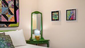 A hotel room with a bed, a green nightstand with a lamp, a mirror, and two framed artworks on the wall. - 2BR/2BA Hot Tub Suite • Coat of Many Colors (Sevierville)