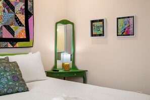 A hotel room with a bed, a green nightstand with a lamp, a mirror, and two framed artworks on the wall. - 2BR/2BA Hot Tub Suite • Coat of Many Colors (Sevierville)