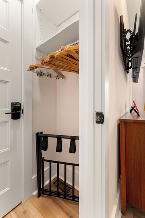 Una habitación con una puerta blanca, un cercado para bebés negro, un perchero de madera y un televisor montado en la pared.