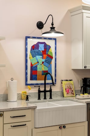 A kitchen with a sink, a faucet, a roll of paper towels, a yellow sponge, a framed quilt, and a cookbook on the counter. - 2BR/2BA Hot Tub Suite • Coat of Many Colors (Sevierville)