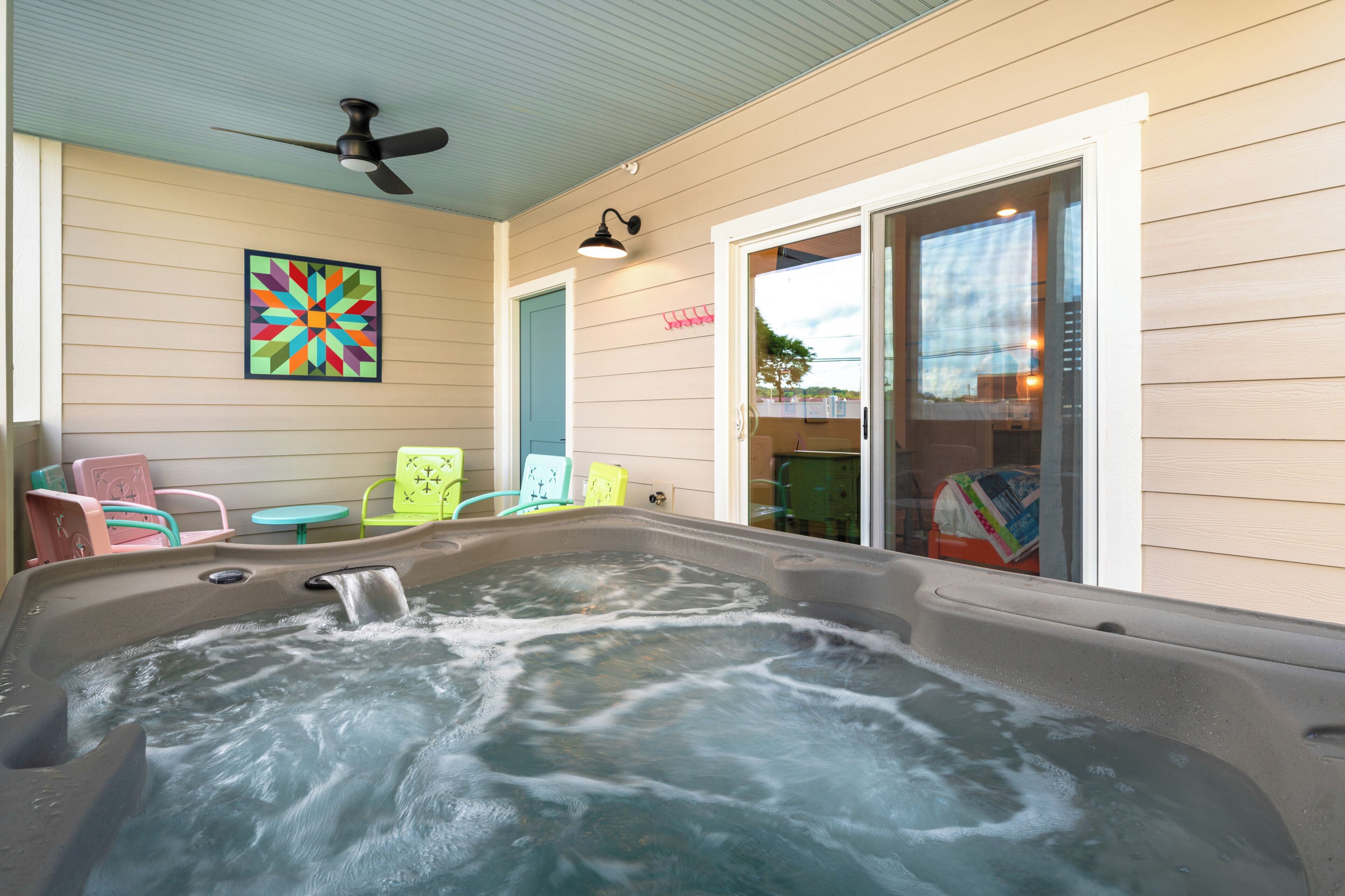 A hot tub with a ceiling fan, colorful chairs, and a door leading to a covered area.