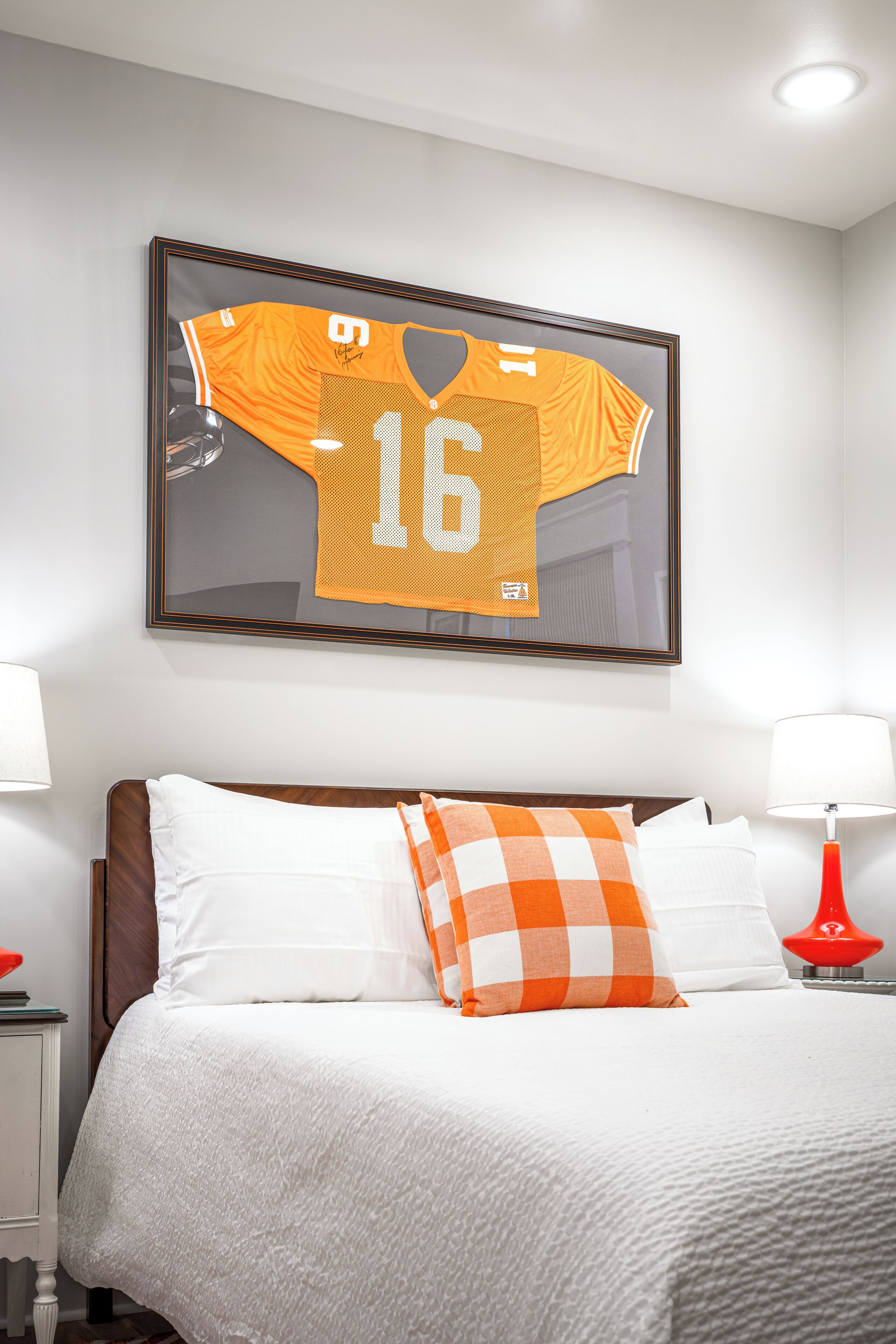A hotel room with a bed, pillows, a framed sports jersey, and bedside lamps.