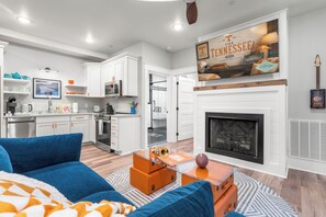 A modern living room with a fireplace, a kitchen with white cabinets, and a mounted sign. - 1BR Hot Tub Suite • Tennessee (Sevierville)