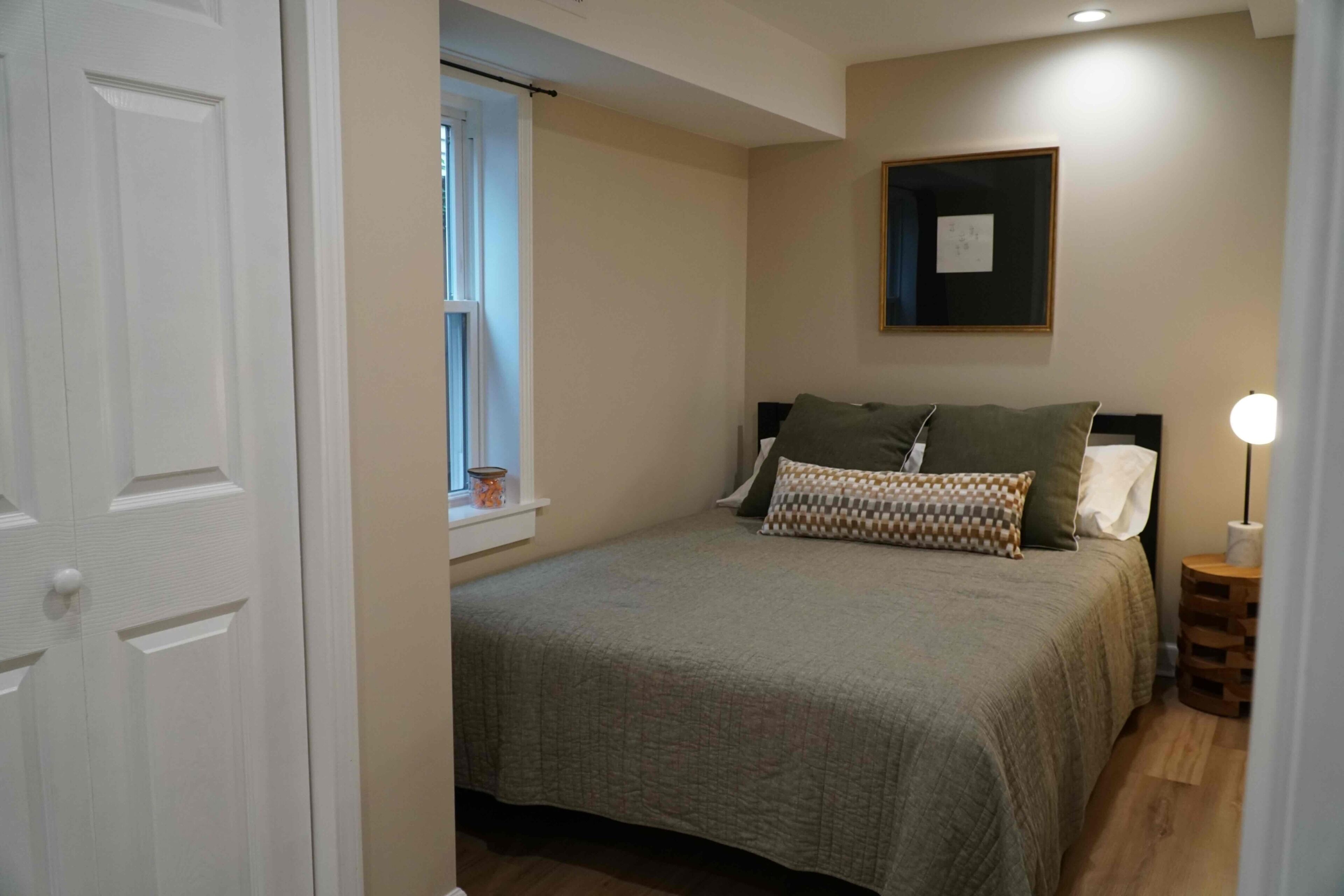 Une chambre à coucher avec un lit, une fenêtre, une lampe de chevet et un tableau encadré au mur.