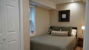 Un dormitorio con cama, ventana, lámpara de noche y un cuadro en la pared.