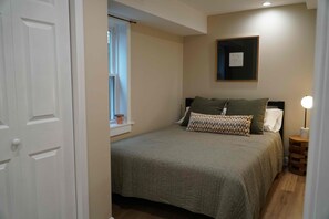 A bedroom with a bed, a window, a bedside lamp, and a framed picture on the wall. - Fully Furnished 2BR. 5-min walk to train. In-unit laundry. Parking Available (Chicago)