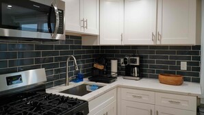 Una cocina moderna con gabinetes blancos, estufa de acero inoxidable, microondas, cafetera y pileta.
