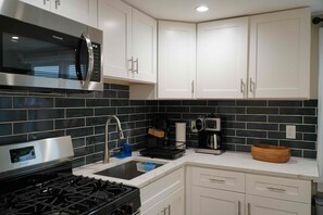 A modern kitchen with white cabinets, a stainless steel range, a microwave, a coffee maker, and a sink. - Fully Furnished 2BR. 5-min walk to train. In-unit laundry. Parking Available (Chicago)