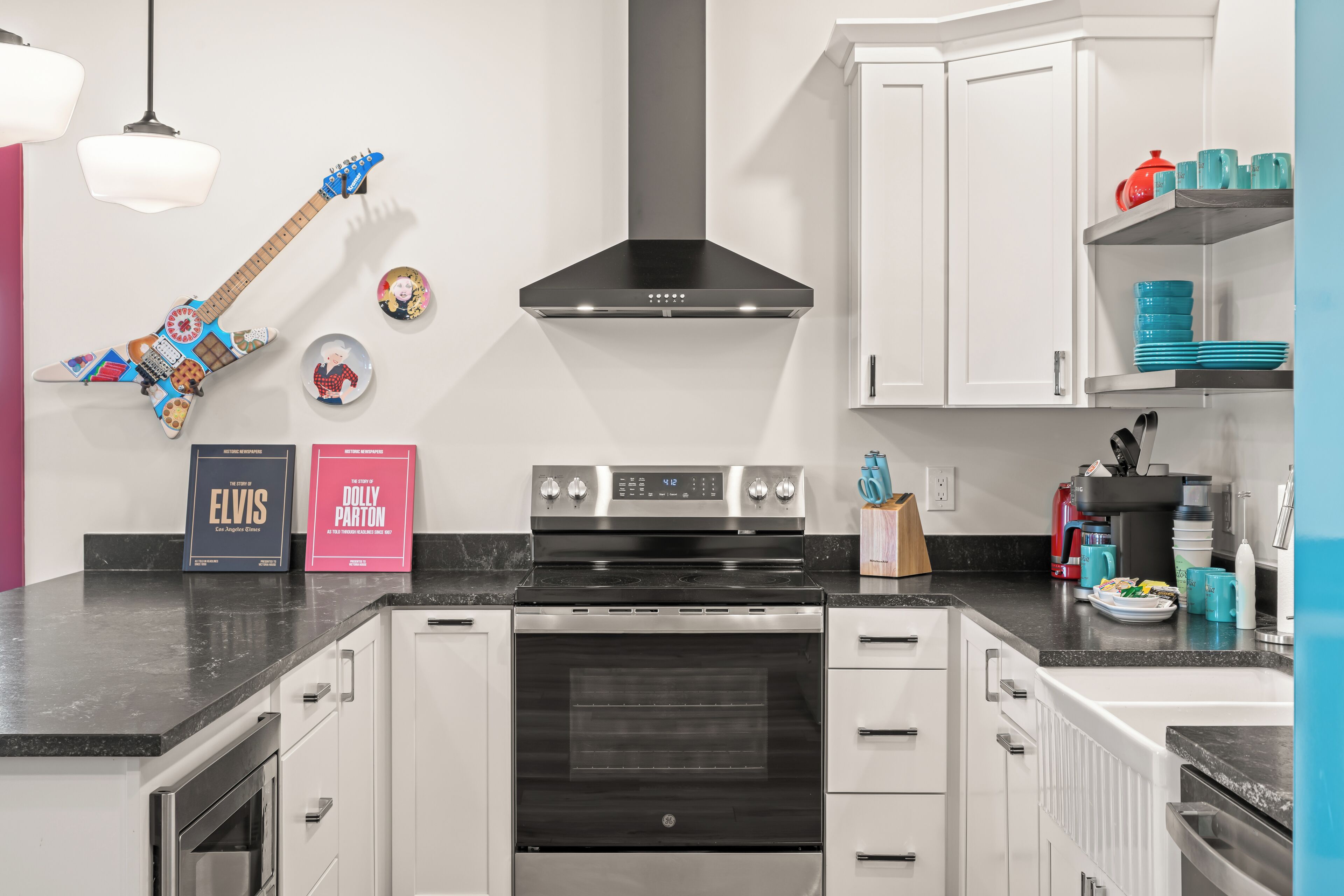A modern kitchen with white cabinetry, a black stove, and a range hood. There are two books on the counter, a guitar, and a red kettle.