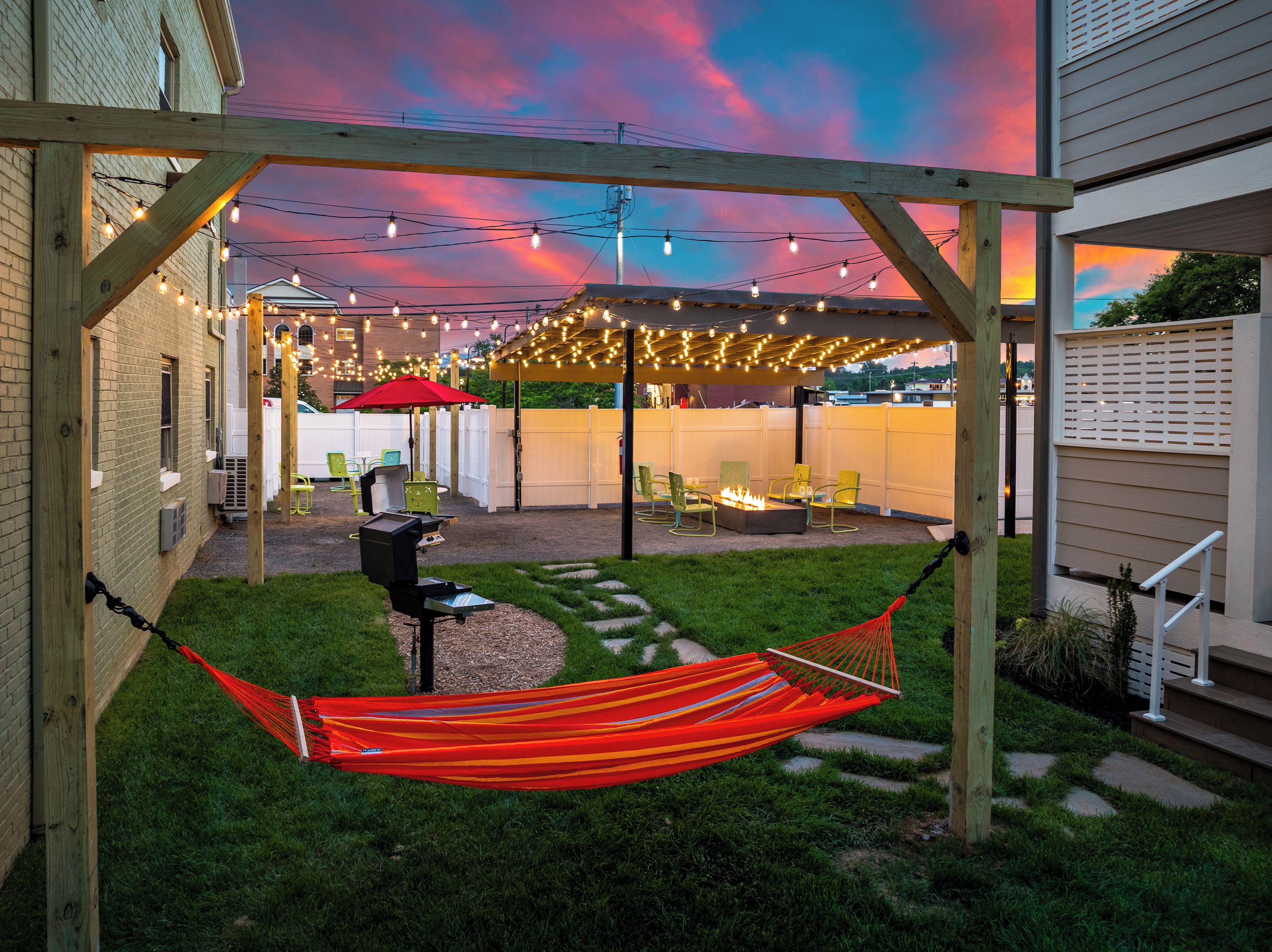 A backyard with a hammock, a barbecue grill, and string lights.