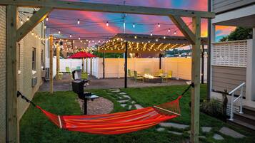 A backyard with a hammock, a barbecue grill, and string lights.