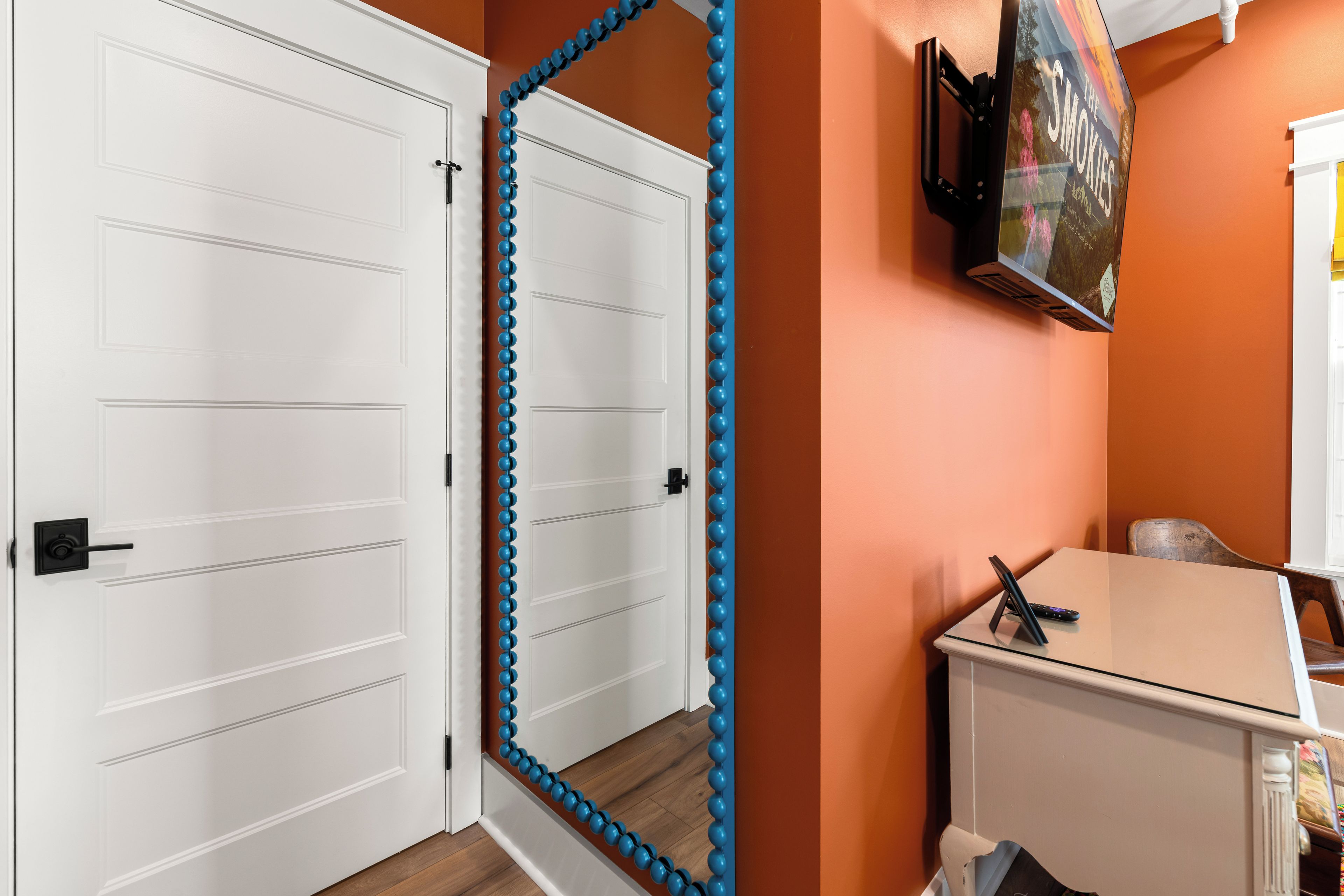 Une pièce avec une porte à deux battants peinte en blanc, un rideau de perles bleu, une armoire blanche et un téléviseur fixé au mur.