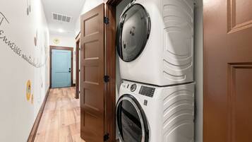 A laundry room with two stacked washing machines, wooden doors, and a hallway with a light blue door at the end.