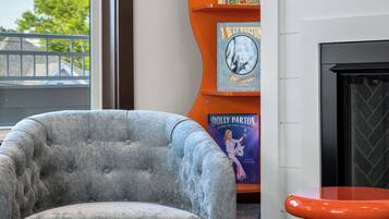 Una sala de estar con un sillón gris, una mesa de centro de vidrio con libros, una estantería naranja y una chimenea.