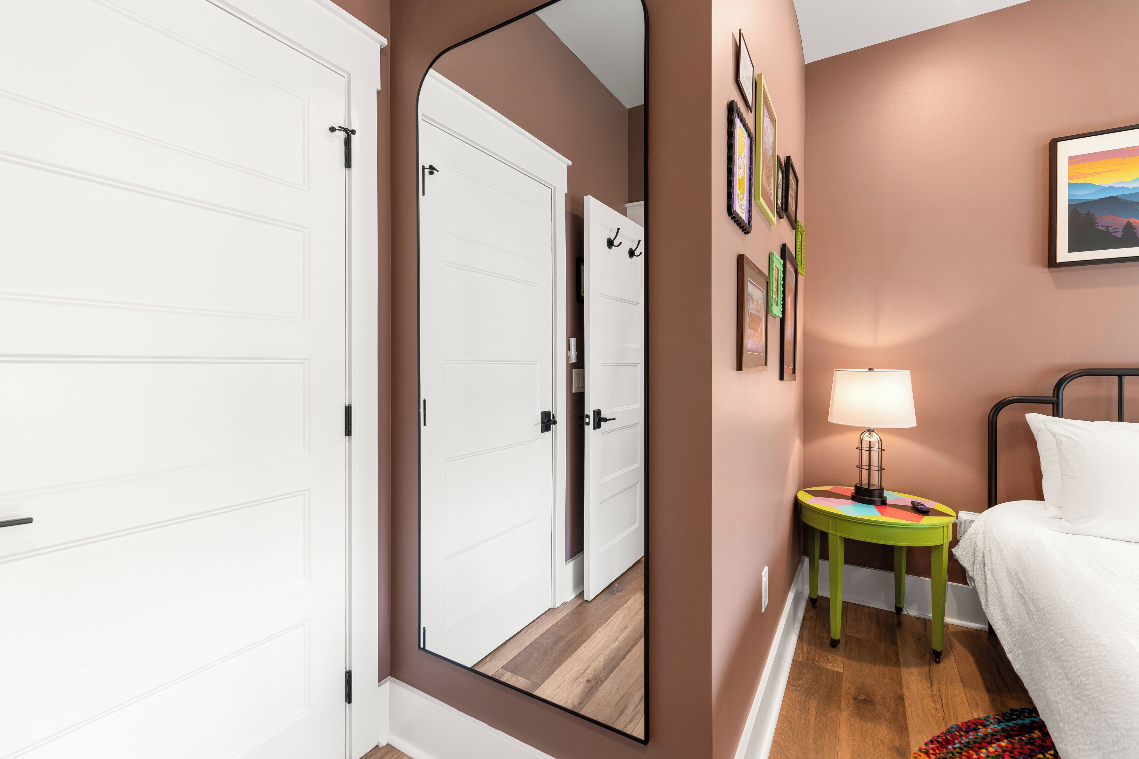 Un dormitorio con cama, una mesita de noche con lámpara, un espejo y una pared con cuadros enmarcados.