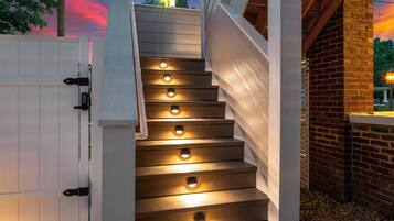 Una escalera de madera con iluminación integrada, una puerta blanca y una pared de ladrillo.