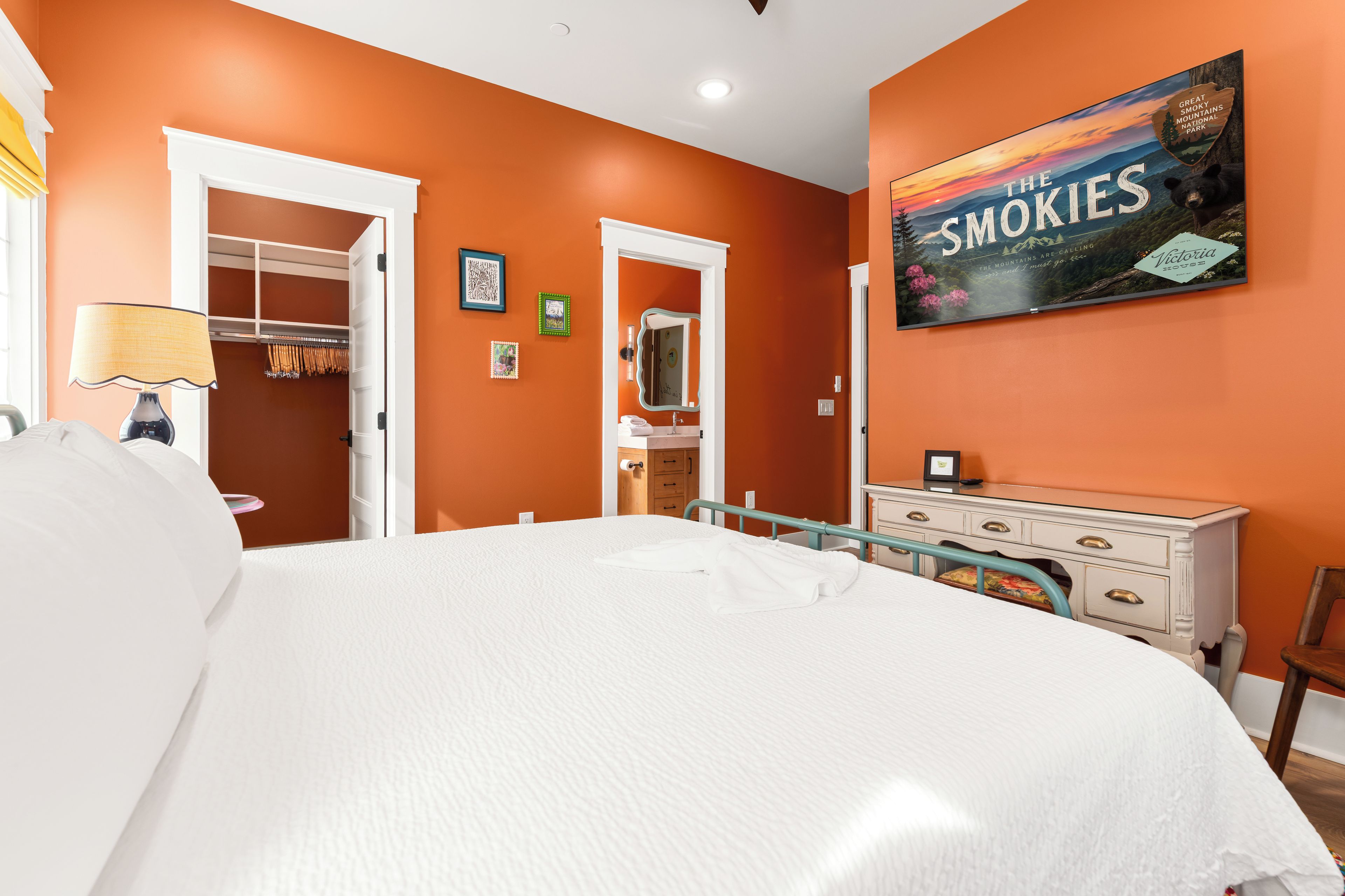 A hotel room with a large bed, a dresser, a mirror, and a wall with a framed picture.