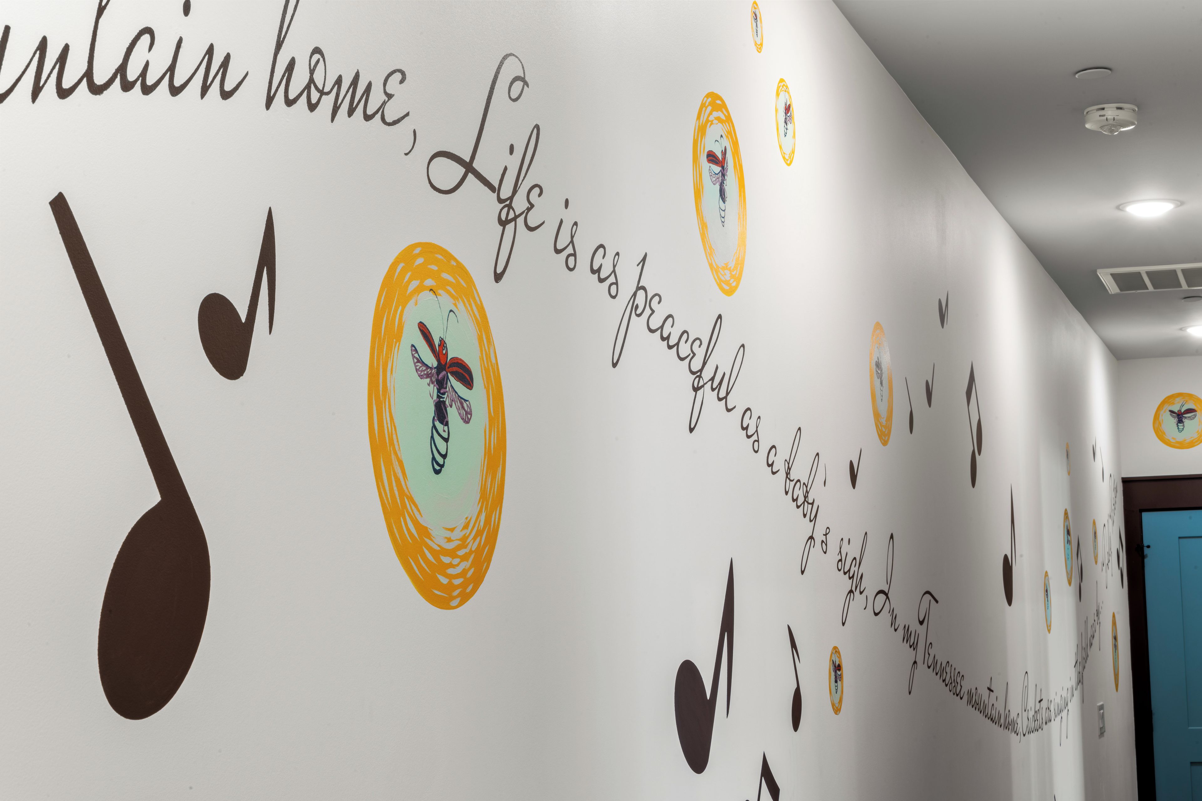 Pared con detalles decorativos, incluyendo notas musicales, una mariposa y texto.