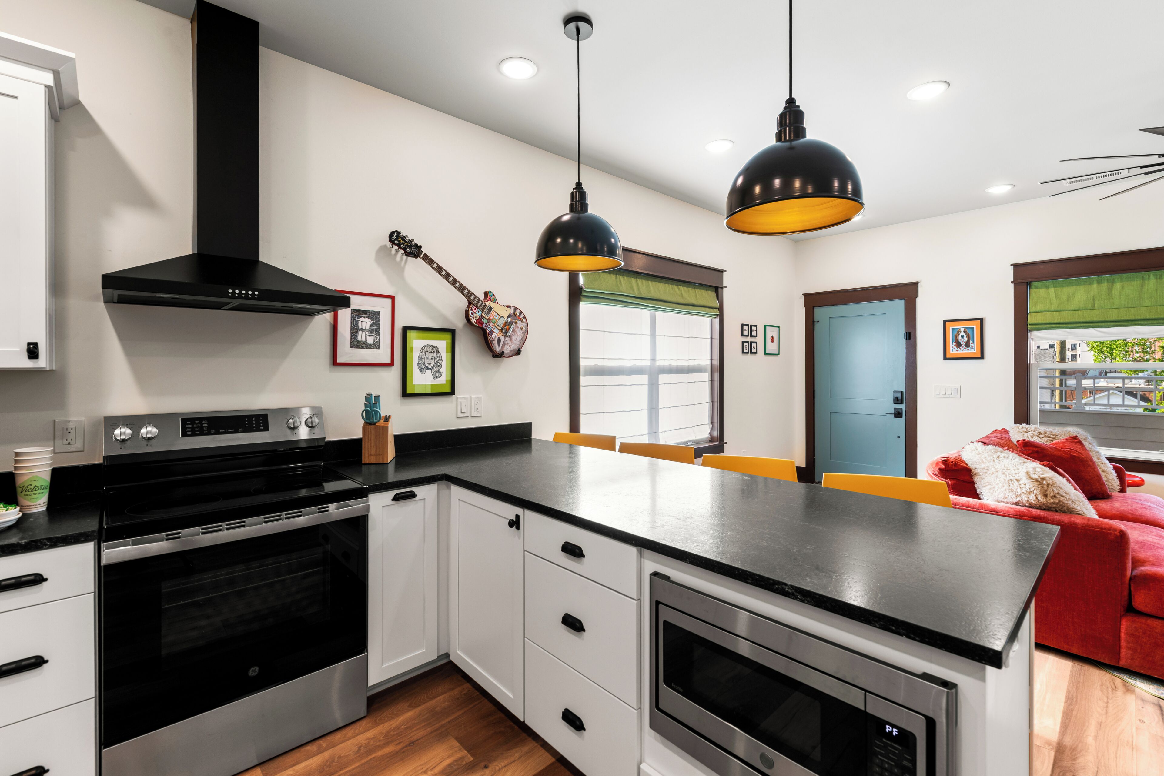 Una cocina moderna con una isla central, electrodomésticos negros y un sofá rojo en la zona de estar contigua.